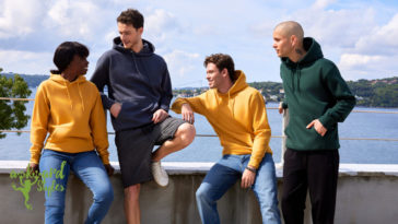 Four young people wearing hoodies sitting on the balustrade of a bridge over sea