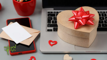 A heart-shaped box with a red bow on a laptop keyboard, accompanied by an envelope, a blank card, and decorative hearts, suggesting a theme of romantic themed gift-giving during Valentine's Day.
