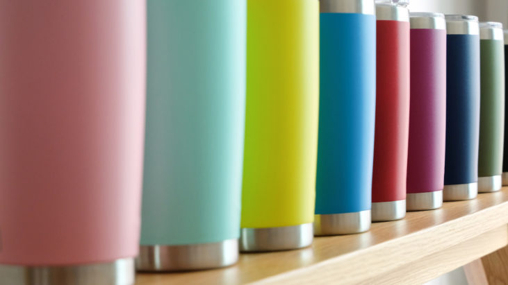a row of colorful stainless steel tumblers on a wooden shelf