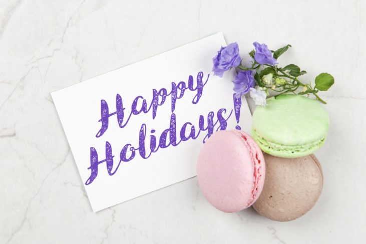 happy holidays message postcard, includes a purple flower and three macarons
